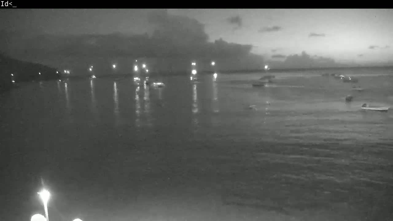 Several boats are moored in calm water at dusk under a partly cloudy sky.