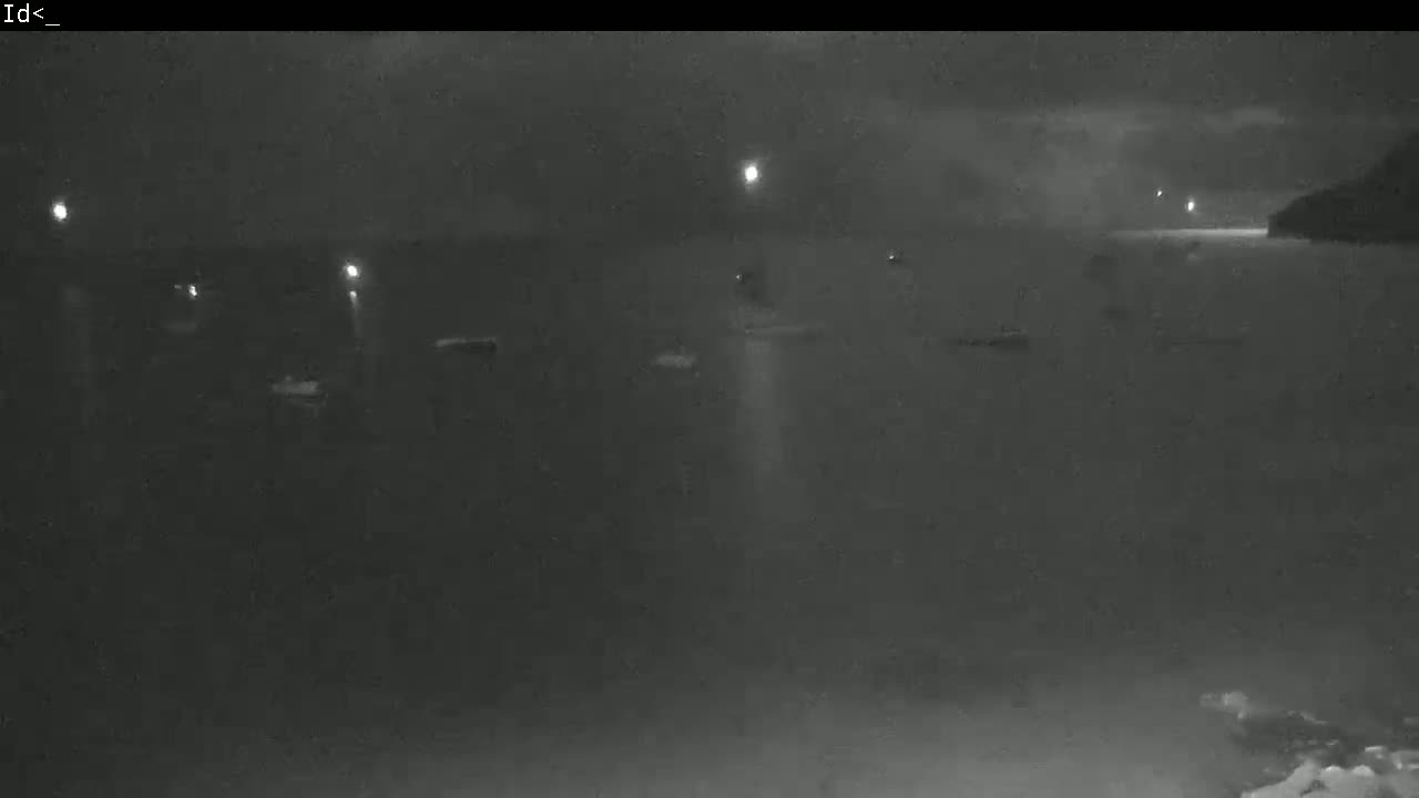 A nighttime, low-light view of several boats at a dark harbor, illuminated by faint lights on shore and possibly on the vessels themselves.