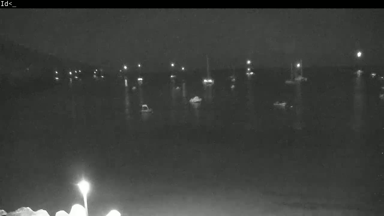 At night, numerous boats with lights are moored in calm water.
