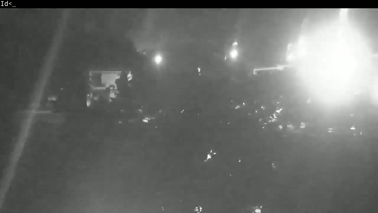A nighttime, low-light image shows indistinct shapes and bright lights in the distance, possibly vehicles or buildings.