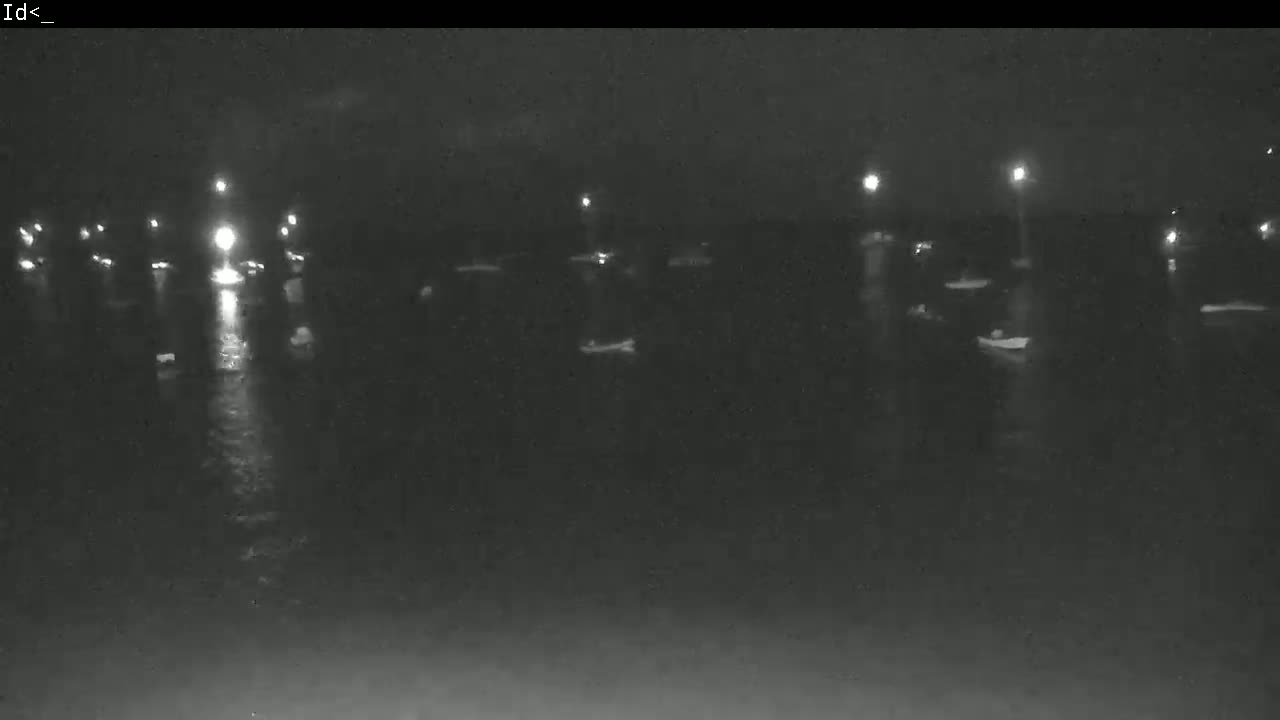 A nighttime, low-light view of several small boats moored at a dock, illuminated by faint lights.