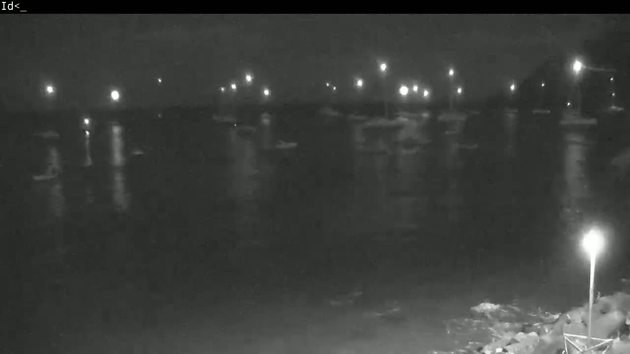 A nighttime, low-light view of a body of water with numerous boats and lights reflecting on the surface.