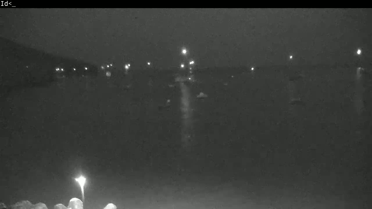 A nighttime, low-light view of a dark body of water with a few distant lights visible on the horizon.