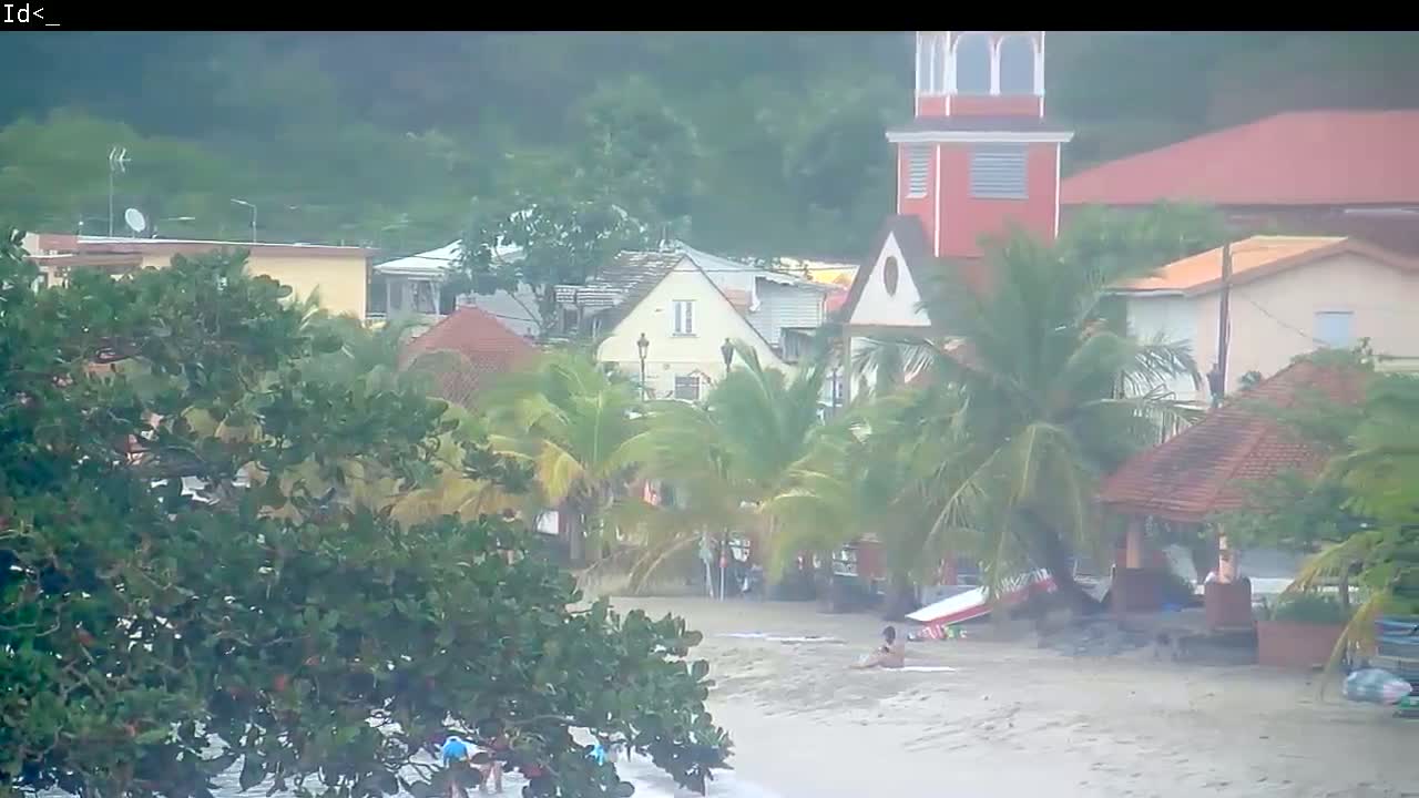 A beach scene shows tropical buildings and palm trees under heavy rain, with a few people visible near the water's edge.