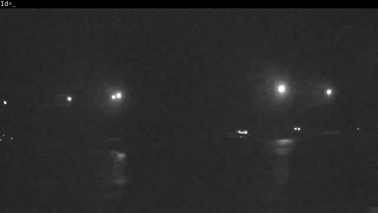 A dark, nighttime scene shows several distant headlights on a wet road illuminated by streetlights.