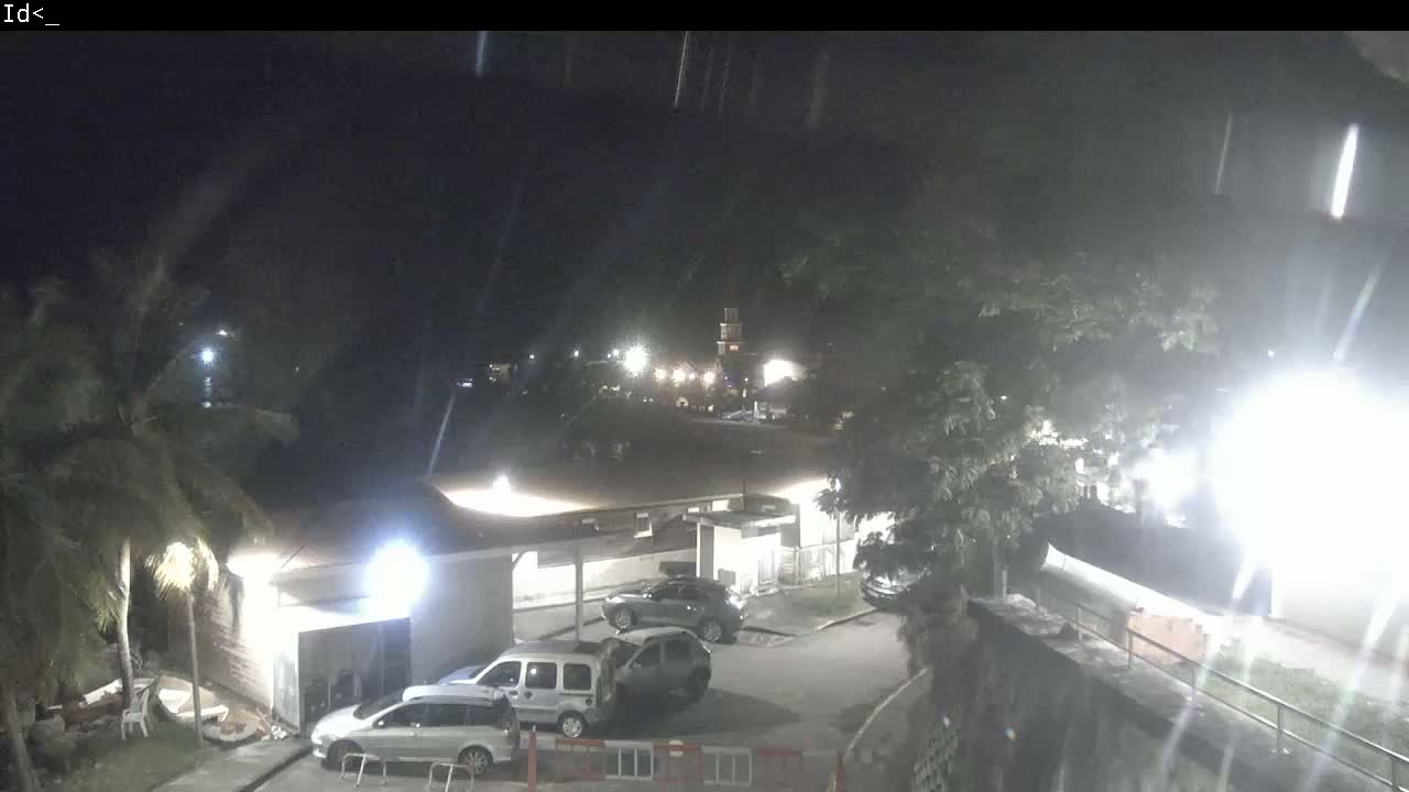 A nighttime, dimly lit parking lot with several cars parked near a building under a slightly hazy sky.