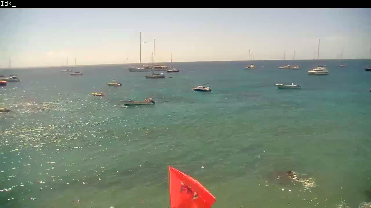 Several boats are anchored in a calm, clear body of water under a sunny sky.