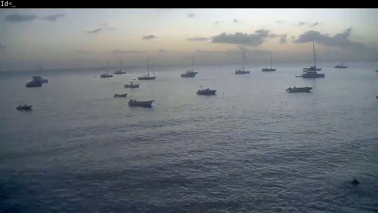 Several sailboats and motorboats are at anchor in calm waters under a mostly cloudy, dusky sky.