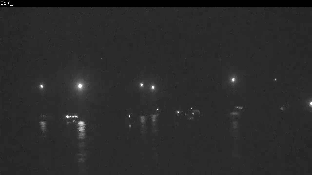 A nighttime view of a wet road with dimly lit vehicles and streetlights.