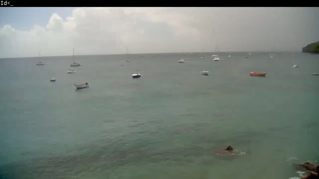 Several boats are anchored in calm, overcast water near a rocky shoreline.