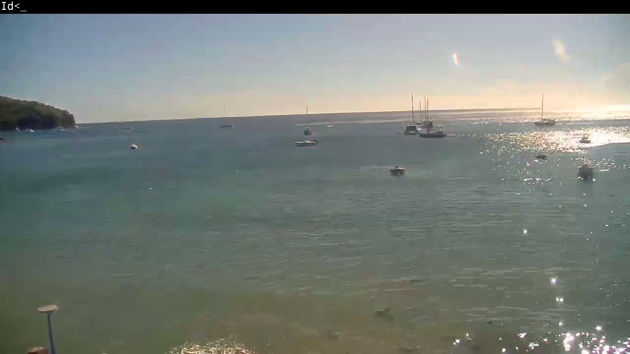 Several boats are scattered across a calm, sunlit body of water near a small, dark-green landmass.