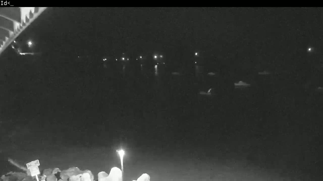 A nighttime, low-light view of a dark body of water with several small, indistinct objects and a few distant lights on the far shore.