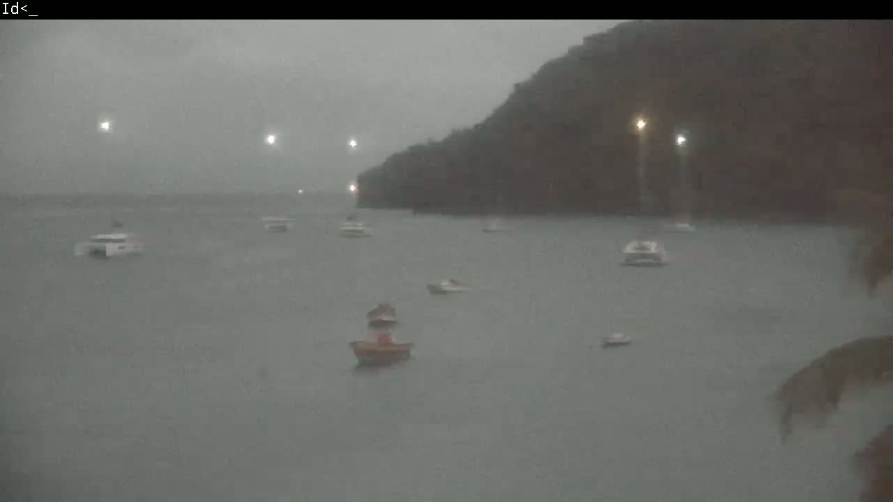 Several boats are anchored in a body of water near a dark, rain-swept shoreline.