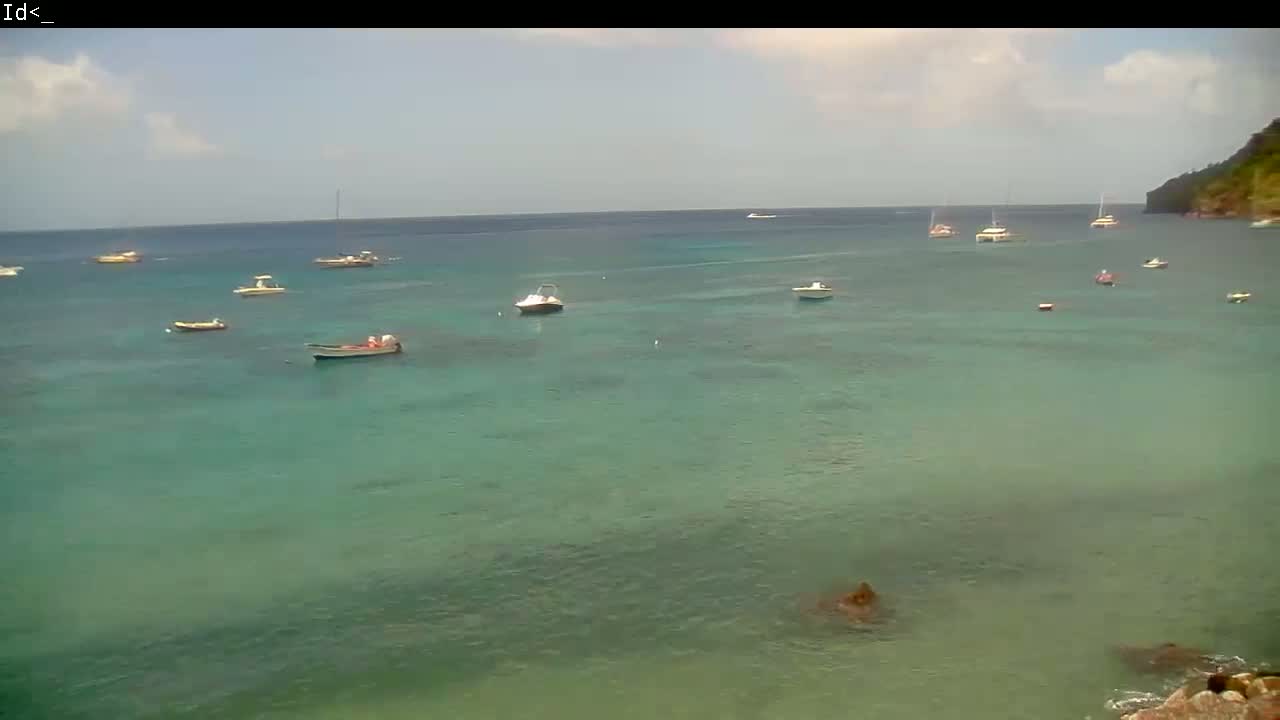 Several boats are scattered across a calm, teal-colored ocean on a partly cloudy day, with a distant shoreline visible.