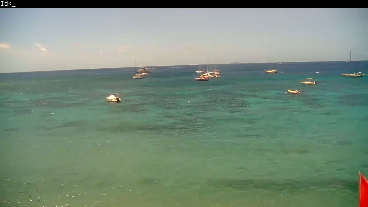 Several boats are anchored in a calm, clear, teal ocean under a mostly sunny sky.