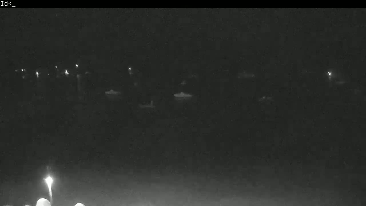 A nighttime, low-light view shows a long line of faintly illuminated objects, possibly boats, on dark water.