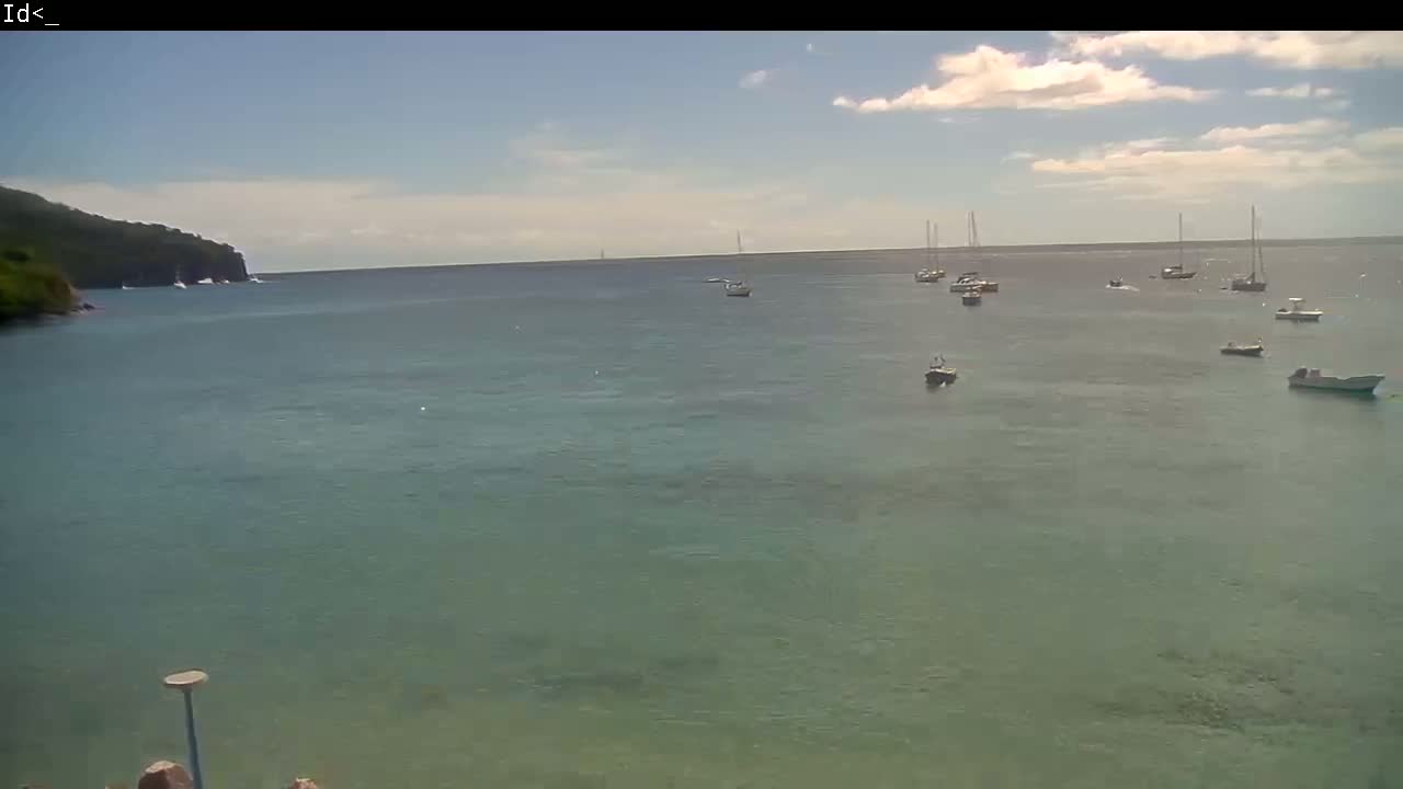 A calm, partly cloudy day shows several boats in a tranquil bay near a dark green, rocky shoreline.