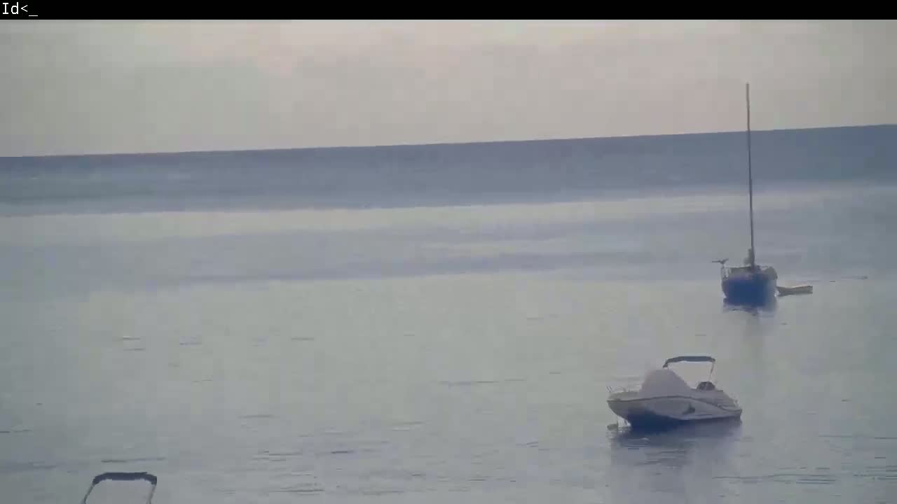 Two small boats are at anchor on a calm, overcast day on a body of water.