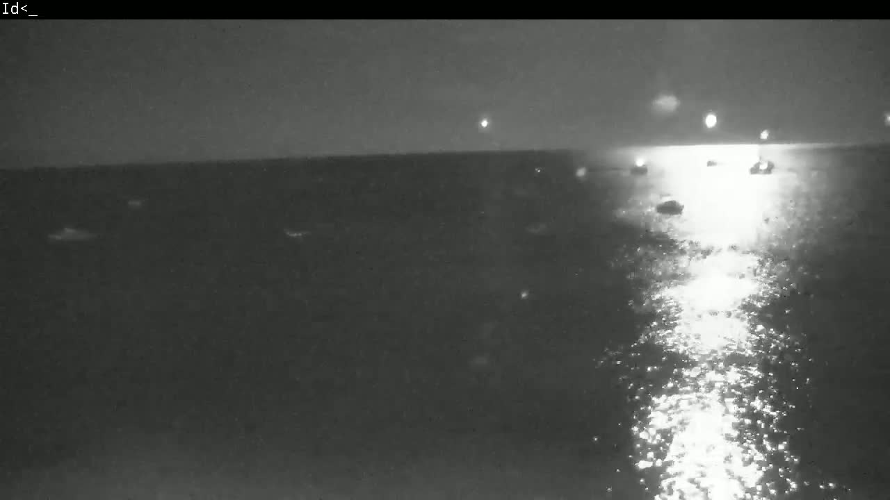 A nighttime, dark view of a body of water with several small lights on the surface, possibly boats, reflecting light on the water's surface.