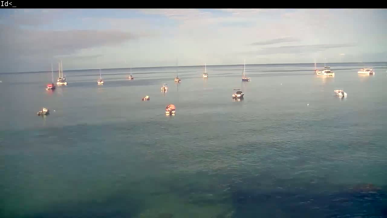 Several boats are anchored in a calm, pale-green body of water under a mostly cloudy sky.