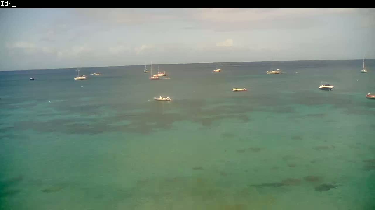 Several boats are anchored in calm, clear, teal-colored water under a mostly cloudy sky.