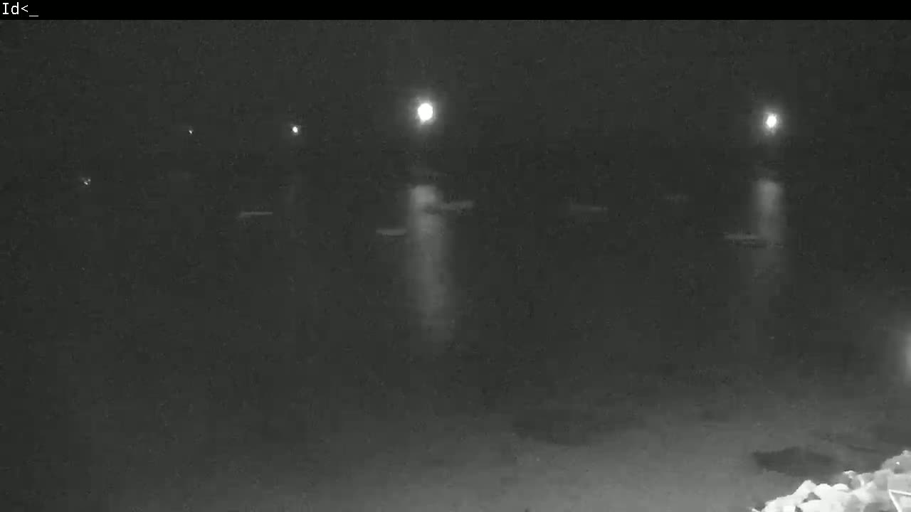 A nighttime, low-light view shows several indistinct objects, possibly boats, illuminated by distant lights on a dark body of water.