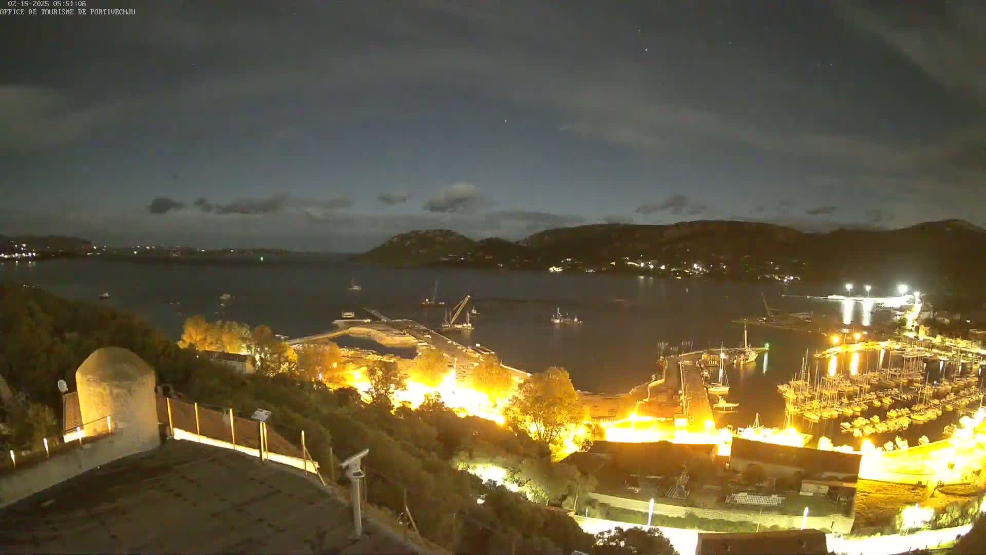 A nighttime, high-angle view of a harbor filled with boats, lit up against a dark sky with a few clouds.