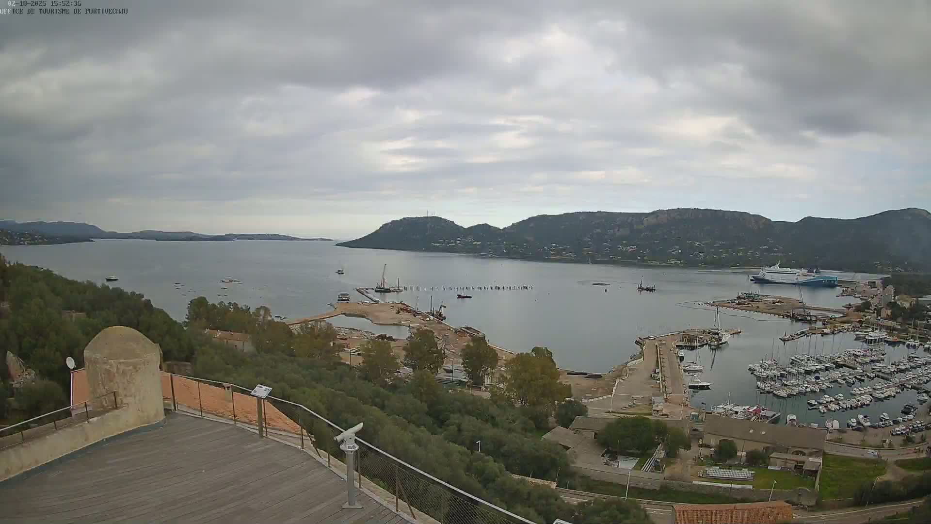 An elevated view of a harbor filled with numerous boats and ships, situated next to a partially constructed area, under an overcast sky.