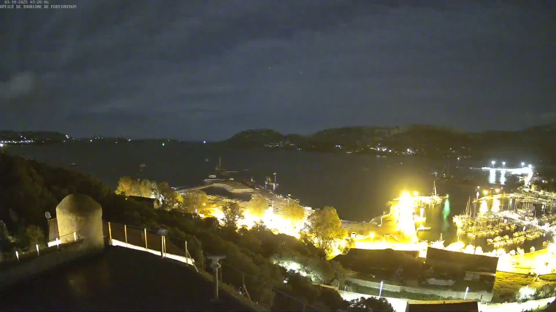 A nighttime view of a harbor filled with boats, illuminated by artificial lights, under a mostly clear sky.
