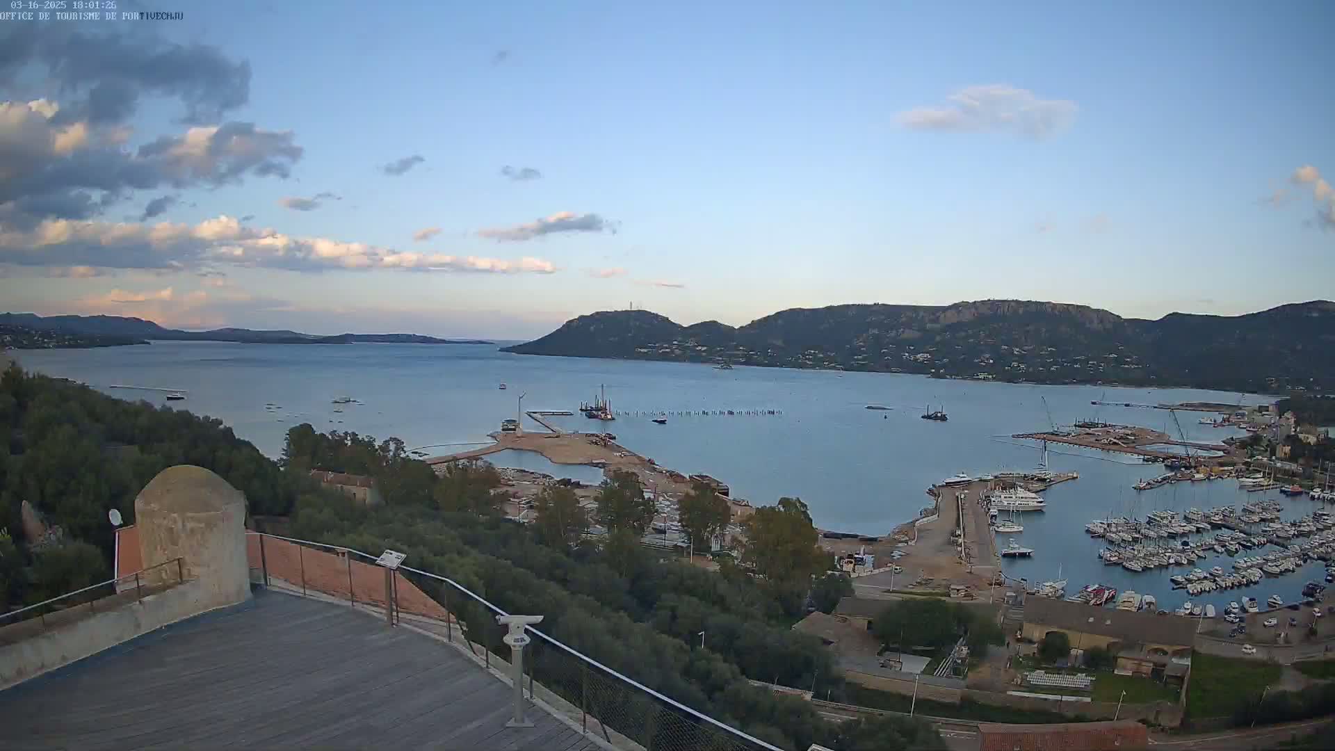 An elevated view overlooking a calm bay with a marina filled with boats, under a partly cloudy sky.
