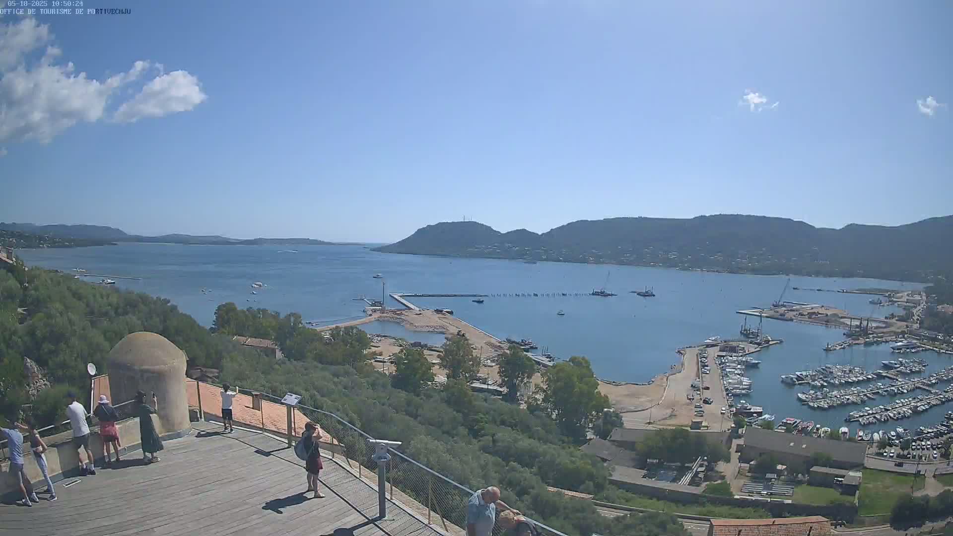 A sunny day overlooking a harbor filled with boats, a small beach, and a town nestled against hillsides.