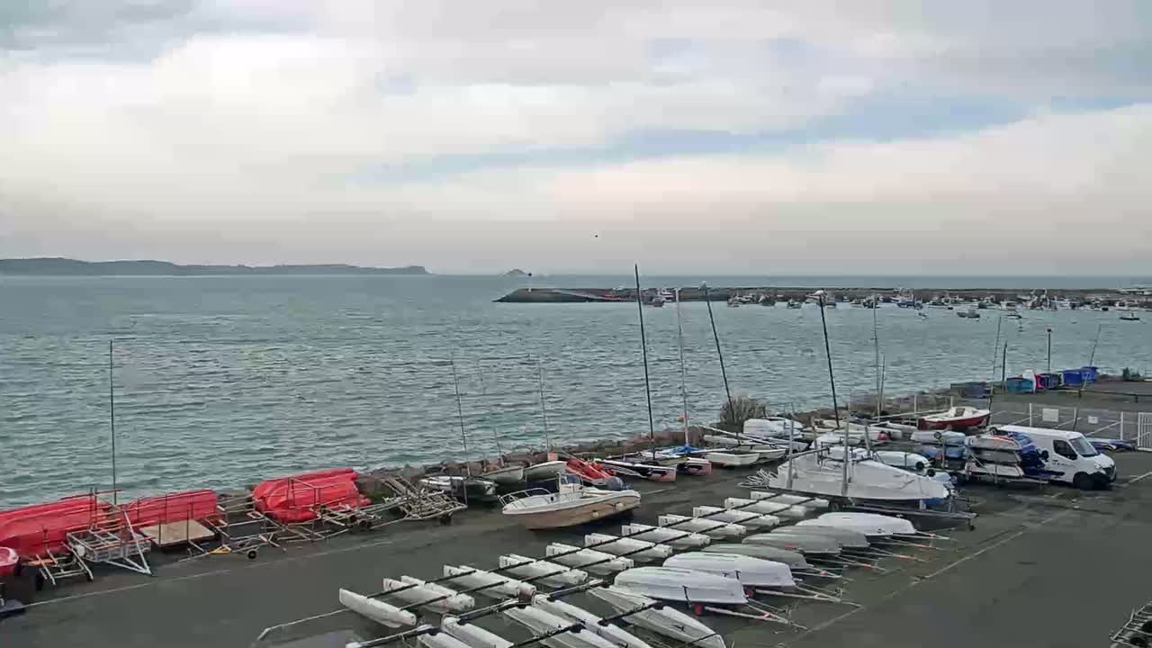 Numerous boats and small sailboats are docked in a harbor on a slightly overcast day with a choppy sea.