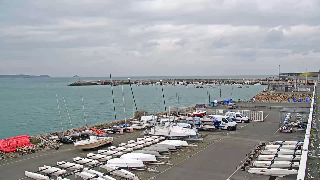 Numerous sailboats and small motorboats are docked in a harbor under an overcast sky.