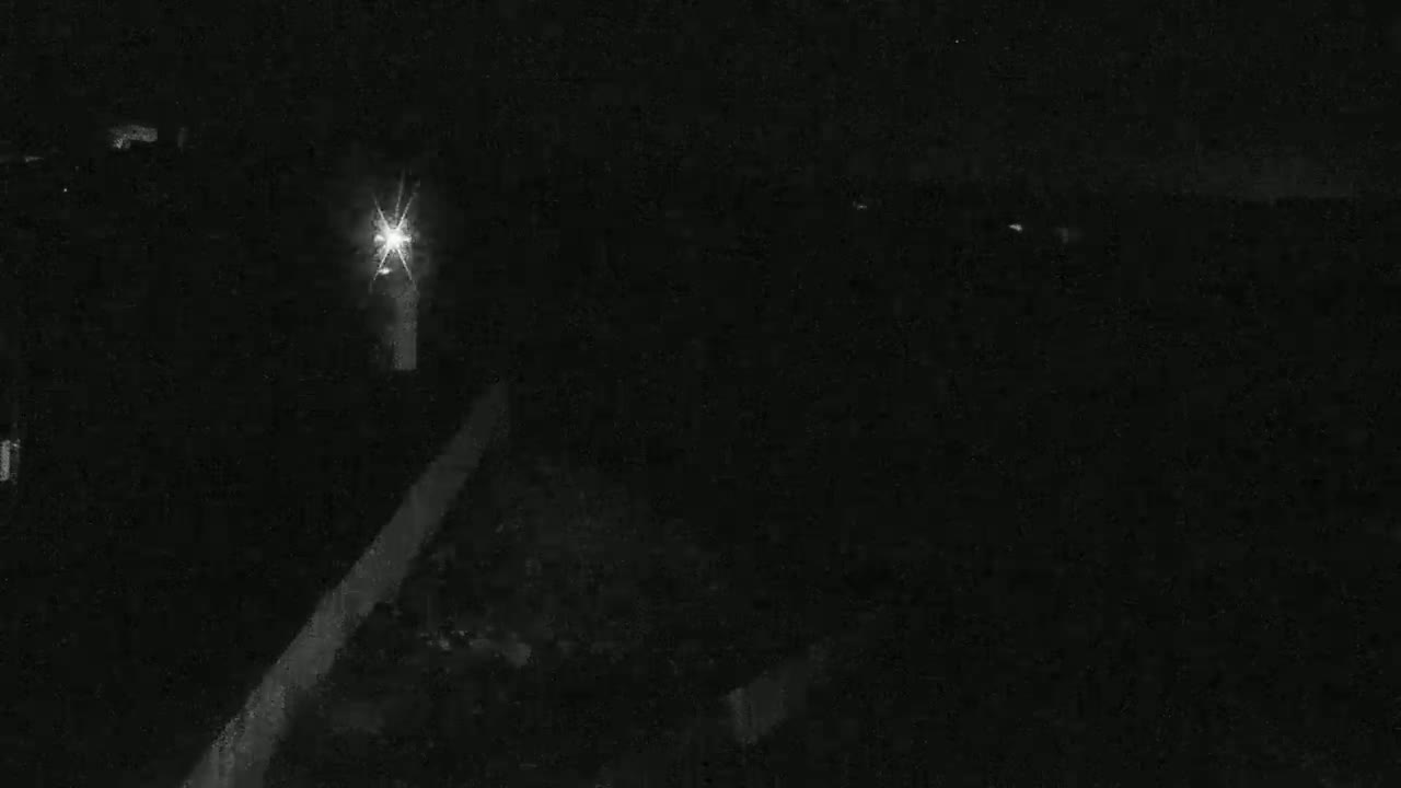 A bright light shines in the darkness of the night, illuminating a portion of a paved surface.