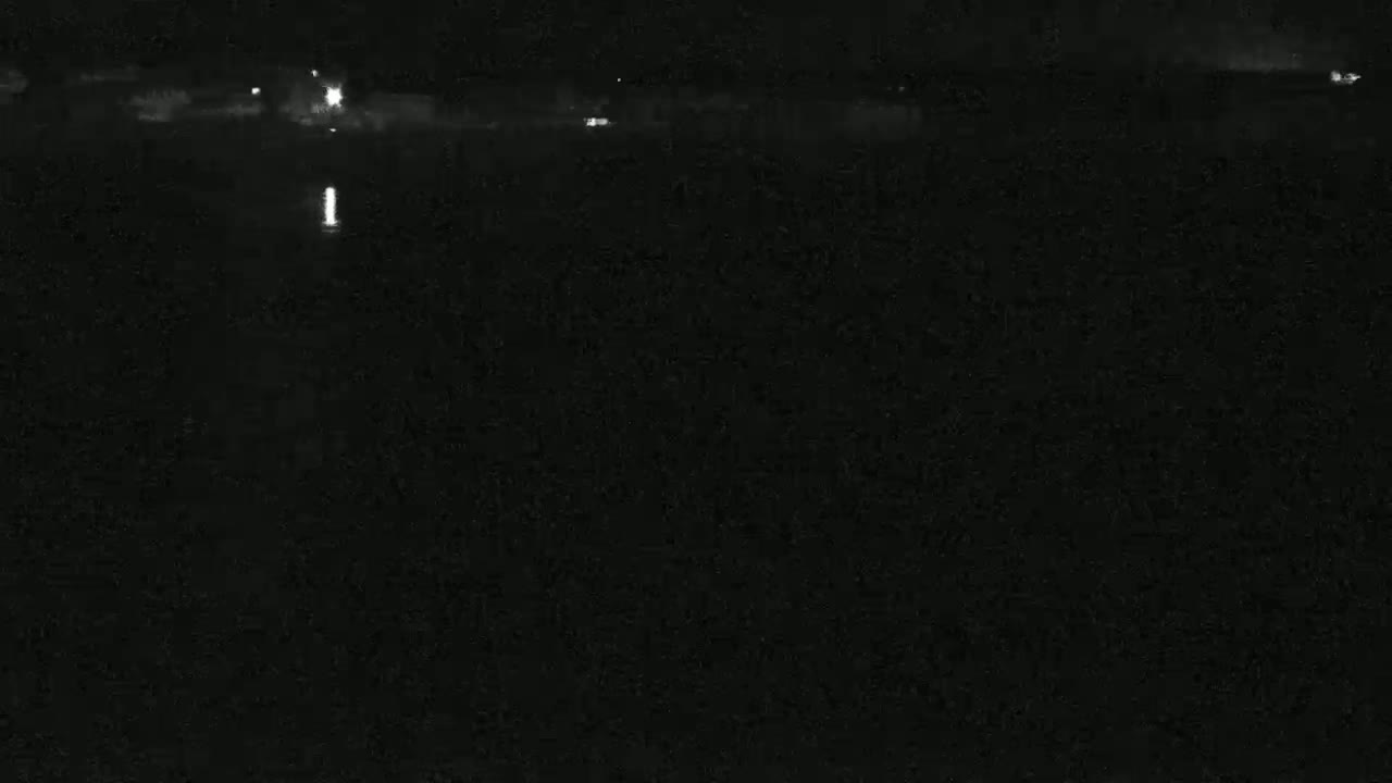 A dark nighttime scene shows a body of water with faint lights visible in the distance.