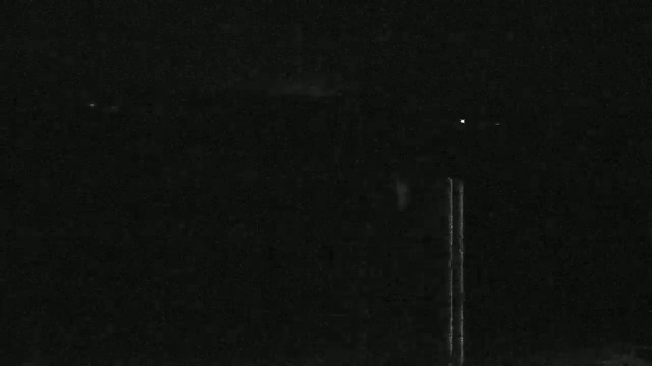 A dark, nighttime scene shows two vertical lines of light against a mostly black background with a few faint lights in the distance.
