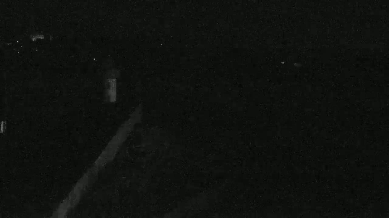 A dark, nighttime scene shows a dimly lit roadway and surrounding dark areas.