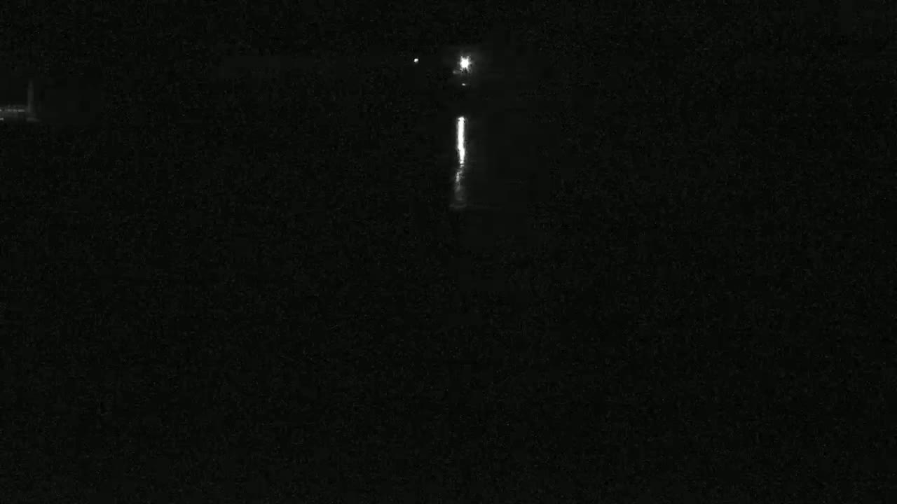 A nighttime, low-light image shows a bright vertical line of light reflecting on dark water under a dark sky.