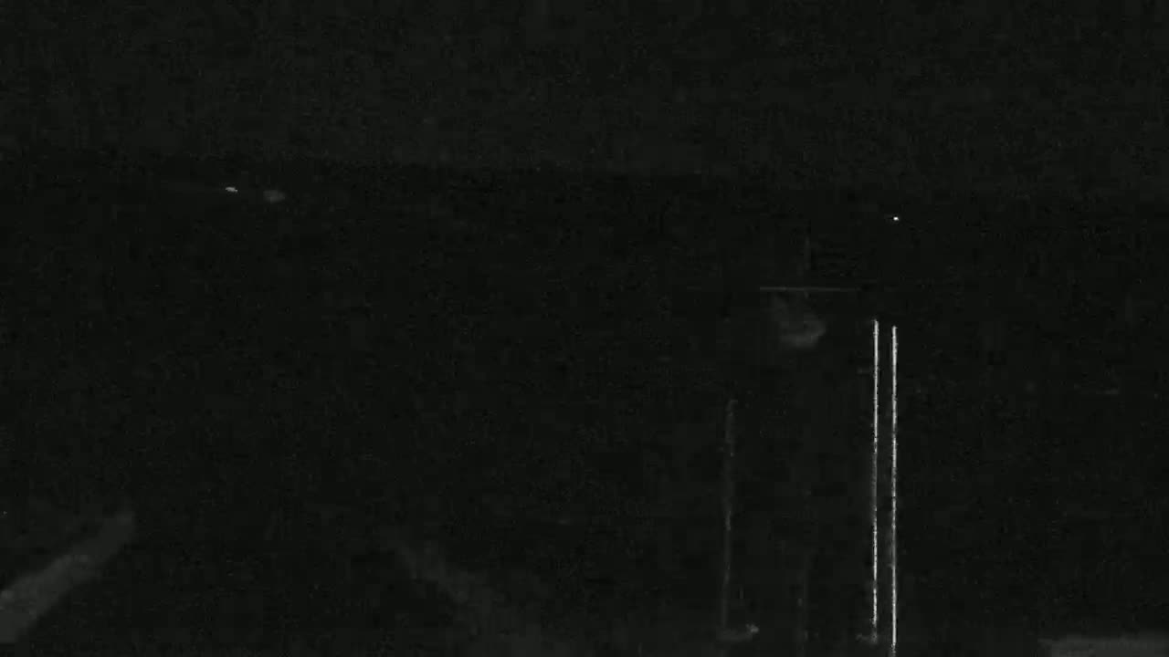 A nearly-black nighttime image shows a blurry, indistinct object and two vertical streaks of light in the center, against a dark background.