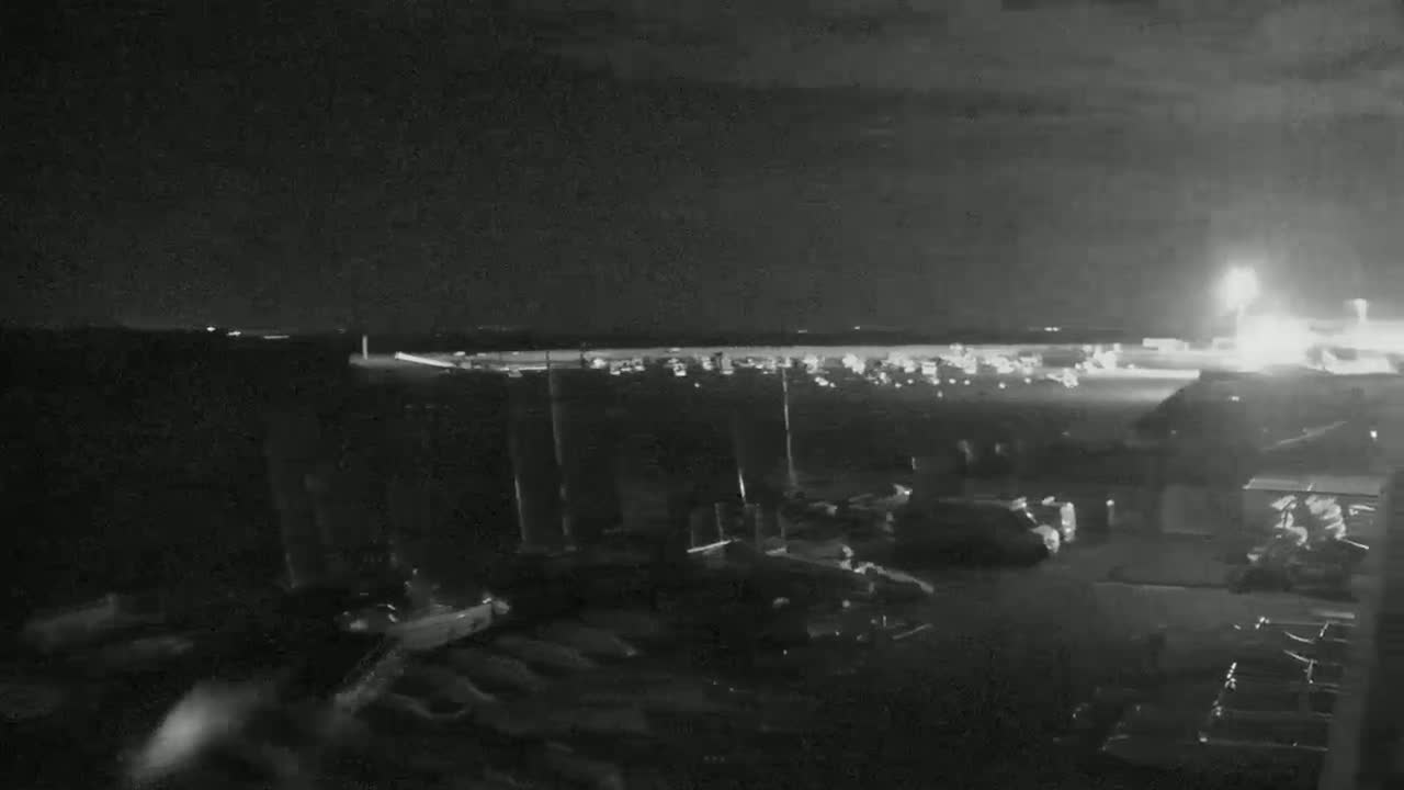 A nighttime view of a parking lot with many vehicles, situated near a brightly lit area that appears to be an airport runway.
