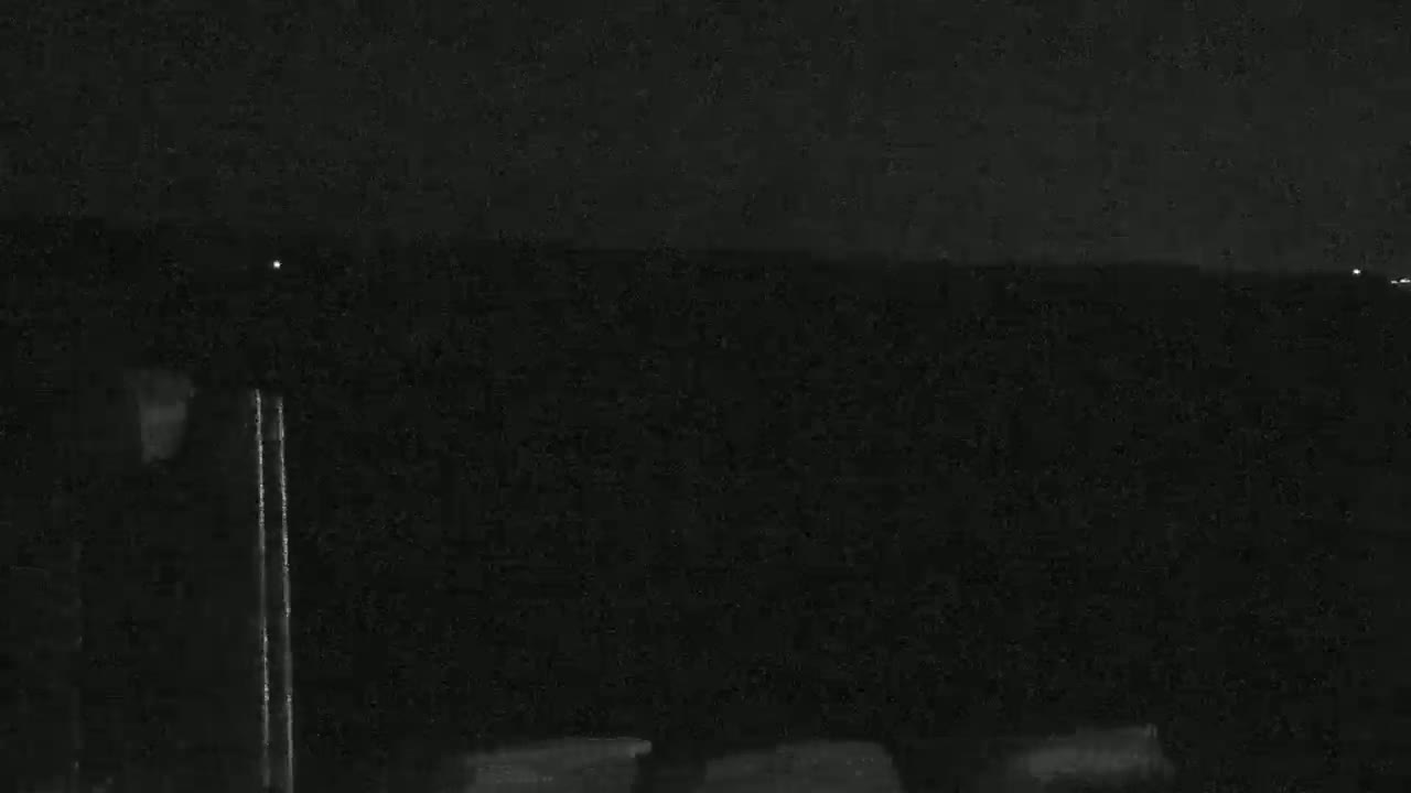 A nighttime, dark image shows a flat, dark landscape with faint, distant lights and two vertical light streaks in the foreground.