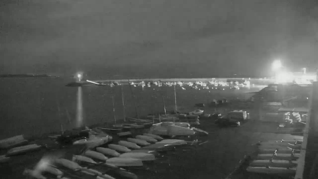 A nighttime, low-light view of a harbor filled with numerous small boats and sailboats, under a dark, cloudy sky.