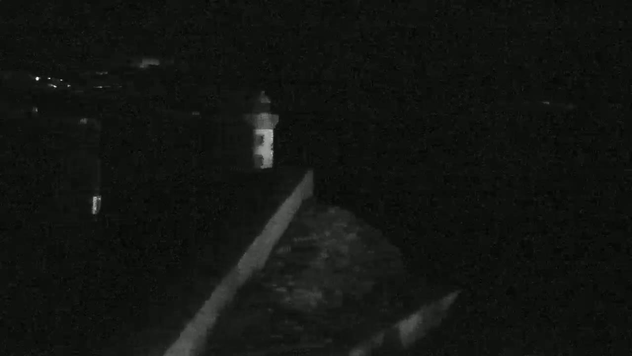 A dimly lit, nighttime scene shows a small structure, possibly a lighthouse, next to a wall or embankment.