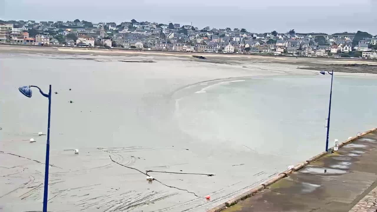 A coastal town is visible across a mostly exposed, light-grey bay under an overcast sky.