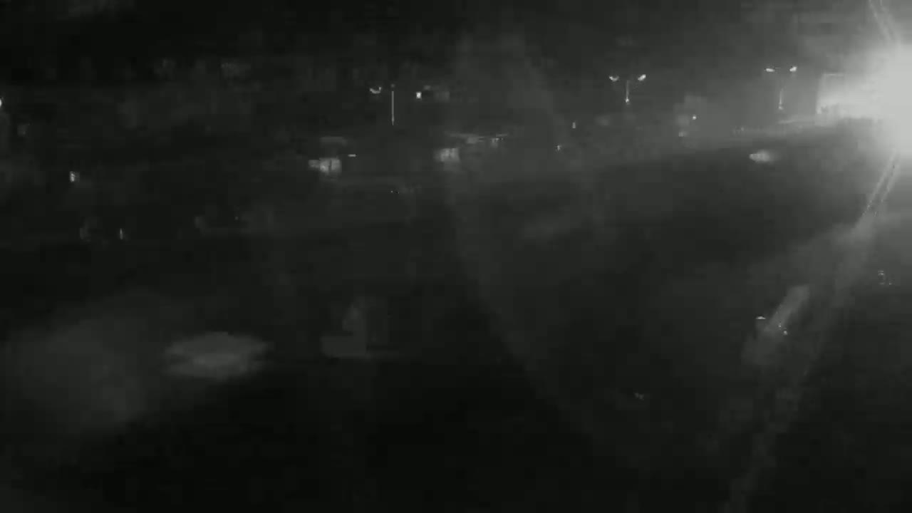 A nighttime, hazy view of a street with dimly lit buildings and vehicles.
