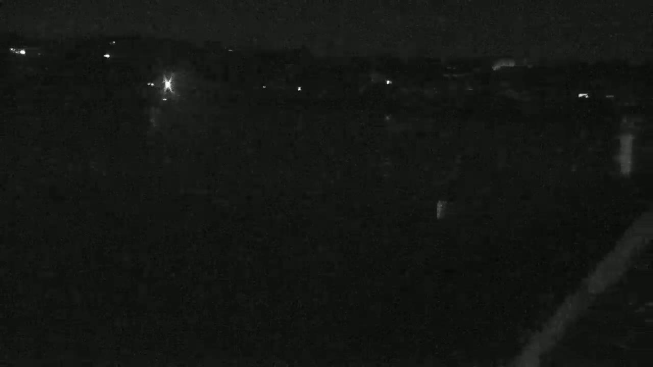 A nighttime, low-light view of a dark landscape with a few scattered lights in the distance.