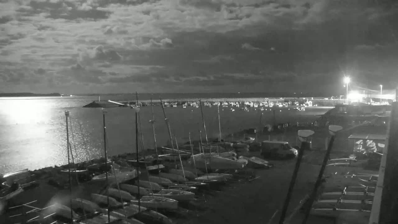 A nighttime view of a harbor filled with sailboats under a cloudy sky.