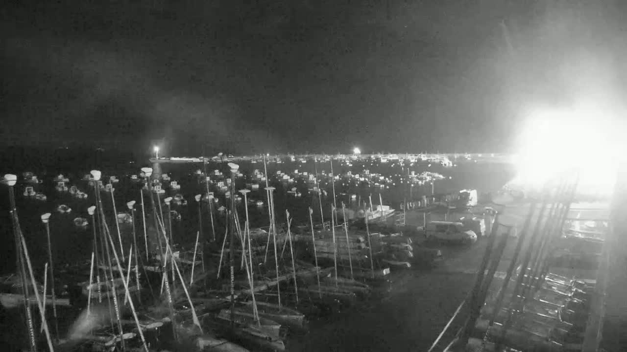 A nighttime, low-light view of a harbor filled with numerous boats moored alongside a dock.