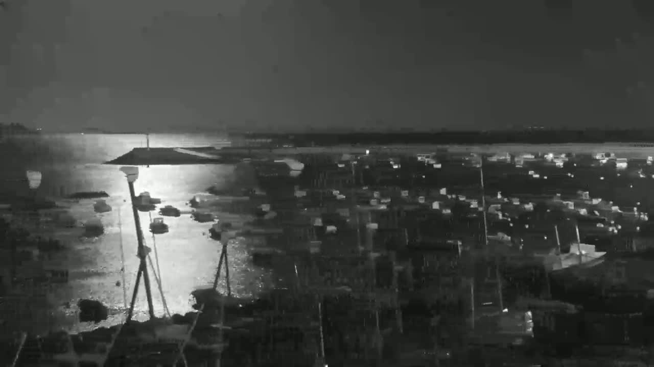 A nighttime, low-light view of a harbor filled with numerous boats, reflecting light on the calm water.