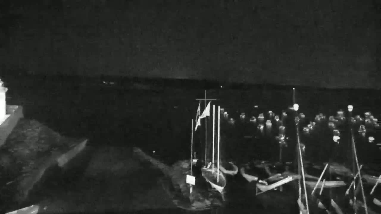 A nighttime, low-light view of a harbor shows several small boats moored at the water's edge.